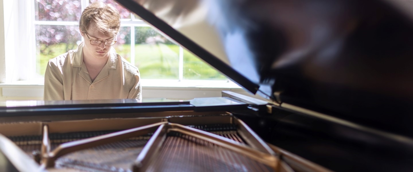 a student playing a grand piano in a sunlit room
