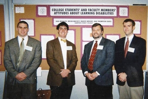 Three students and their professor standing in front of their poster presentation