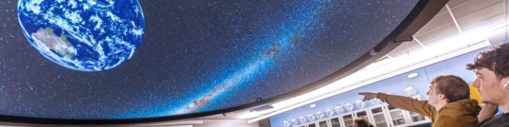 professor and students looking at a planetarium with earth displayed on it