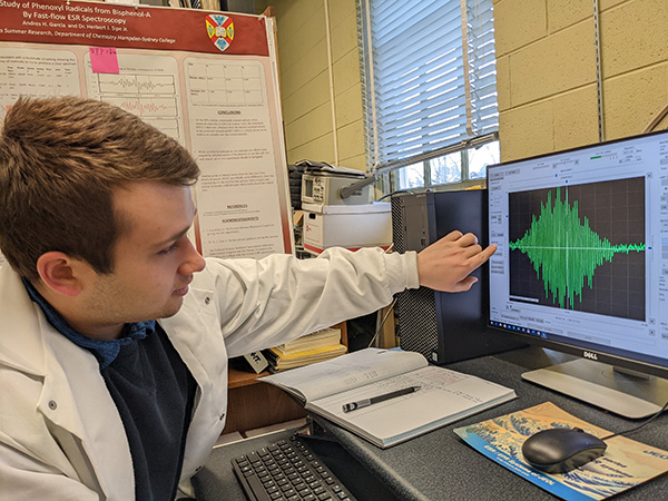 A student in a lab coat pointing to a graph on the computer screen