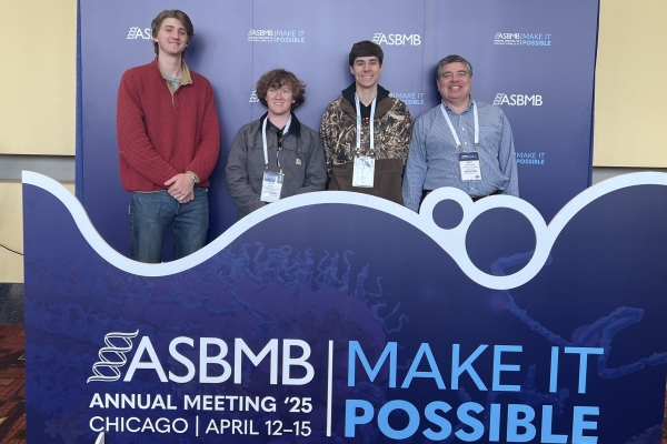 students and professor pose in a group at a conference